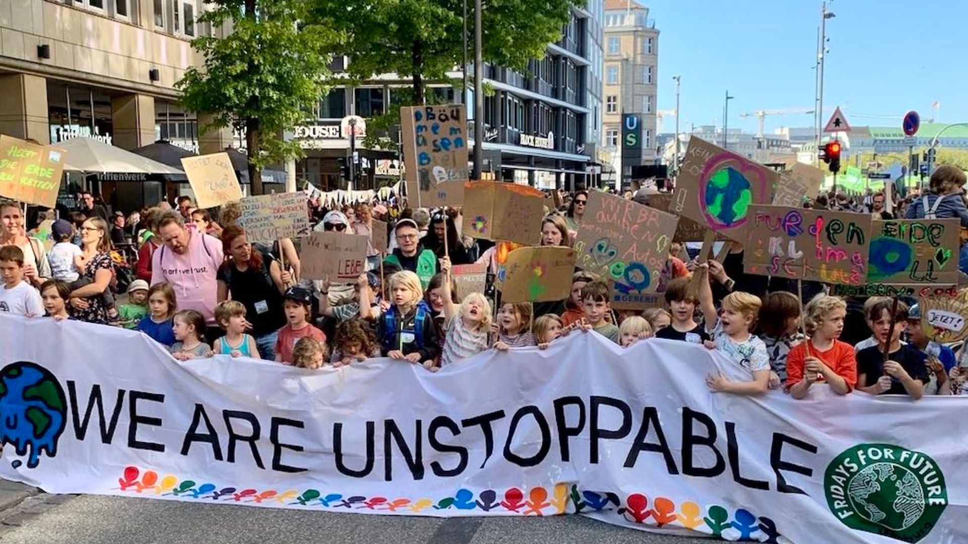 Foto der Kinder- und Familien mit bunten, selbst gebastelten Plakaten und Frontbanner &quot;We are unstoppable&quot;, die den Demozug anführen.