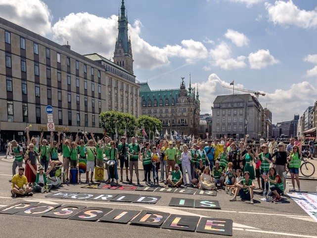 Gruppenbild der Aktionsteilnehmenden vor dem Hamburger Rathaus mit dem Schriftzug &quot;Another World is Possible&quot;